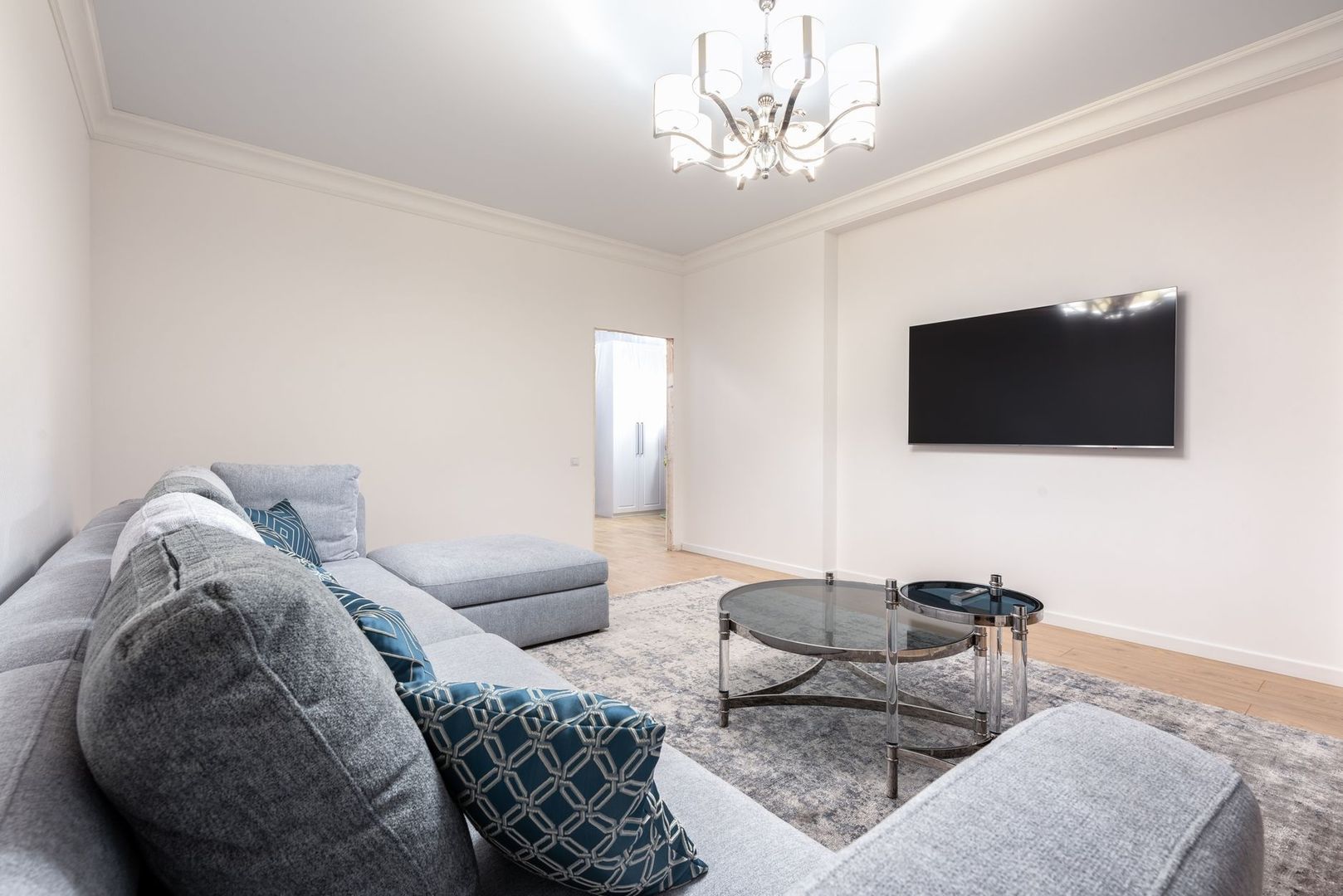 Helles Wohnzimmer mit Sofa, Fernseher und eleganter Deckenleuchte